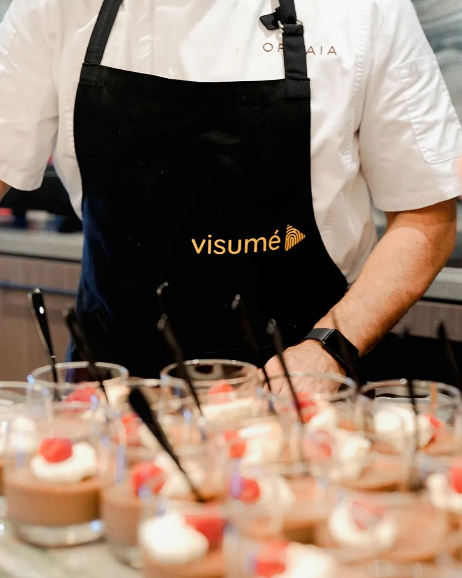 Rows of desserts in glasses, served by a chef in a Visumé apron